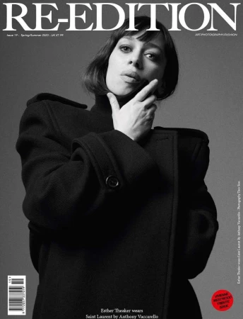 Portrait of a woman wearing a heavy black structured coat against a plain grey backdrop for a magazine cover.