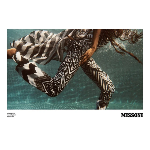 Woman in patterned pants swims underwater in a pool. Fashion shot with summer 2022 branding of Alicante, Spain, and the Missoni logo.