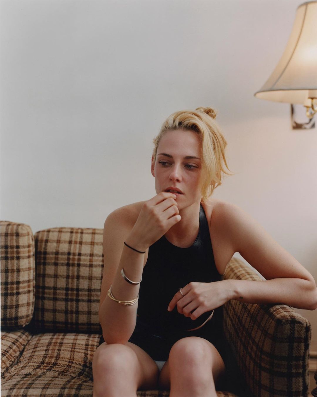 Kristen Stewart seated on a plaid sofa wearing a black top, photographed by Theo Wenner in New York.