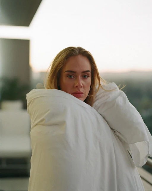 Close-up portrait of a woman wrapped in a white comforter, with blurred background scenery.
