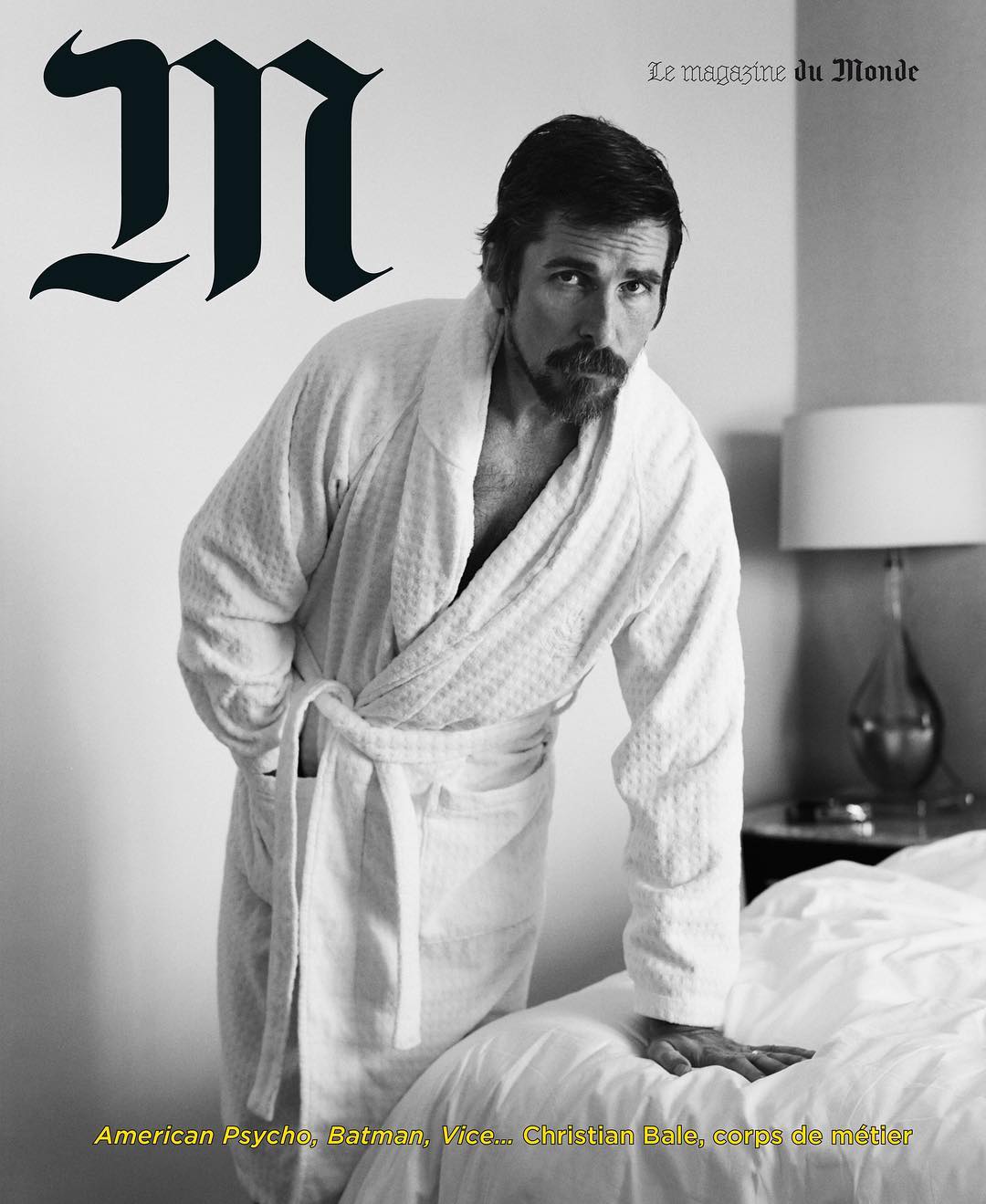 Magazine cover featuring Christian Bale in a white bathrobe leaning on a bed in a neutral-toned interior with magazine text.