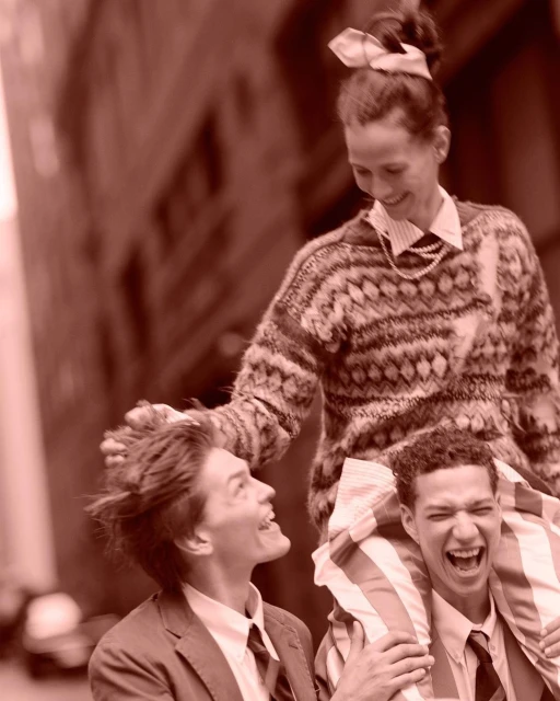 Three smiling people pose outdoors in a cheerful group shot. One woman stands and two men, wearing suits, are positioned below her.