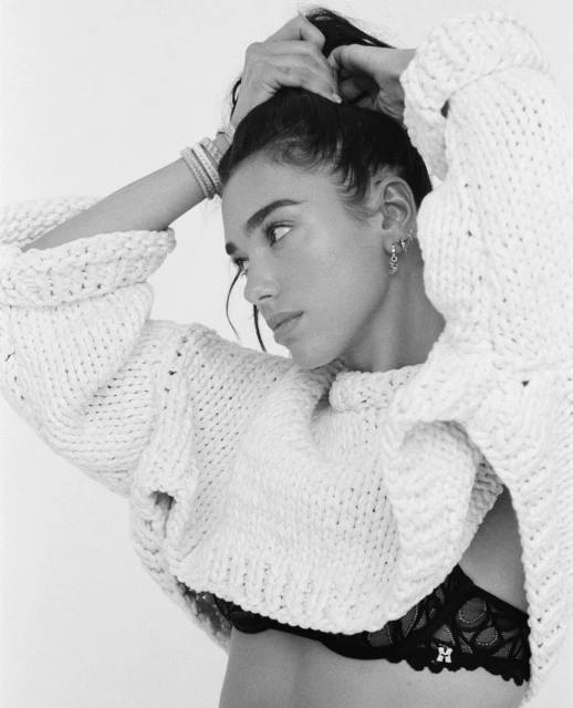 Monochrome portrait of a woman with dark hair, wearing a knit sweater and black lace bra against a white background.