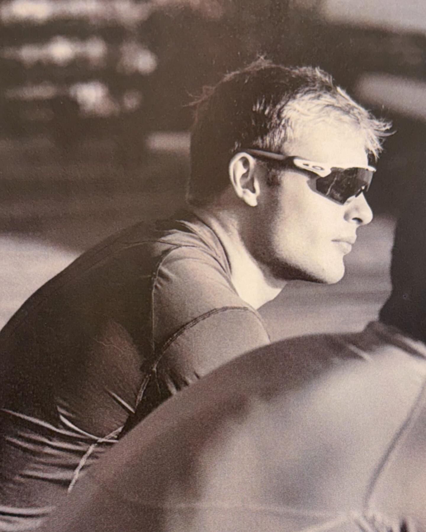 Monochromatic portrait of an adult male wearing sunglasses, gazing to the side with a neutral expression and a blurred background.