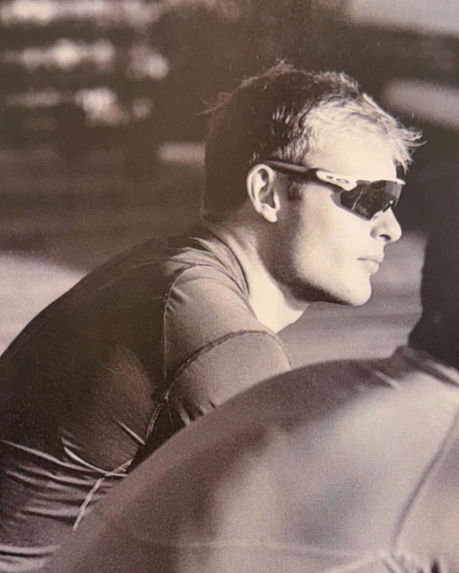 Monochromatic portrait of an adult male wearing sunglasses, gazing to the side with a neutral expression and a blurred background.