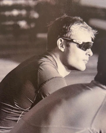 Monochromatic portrait of an adult male wearing sunglasses, gazing to the side with a neutral expression and a blurred background.