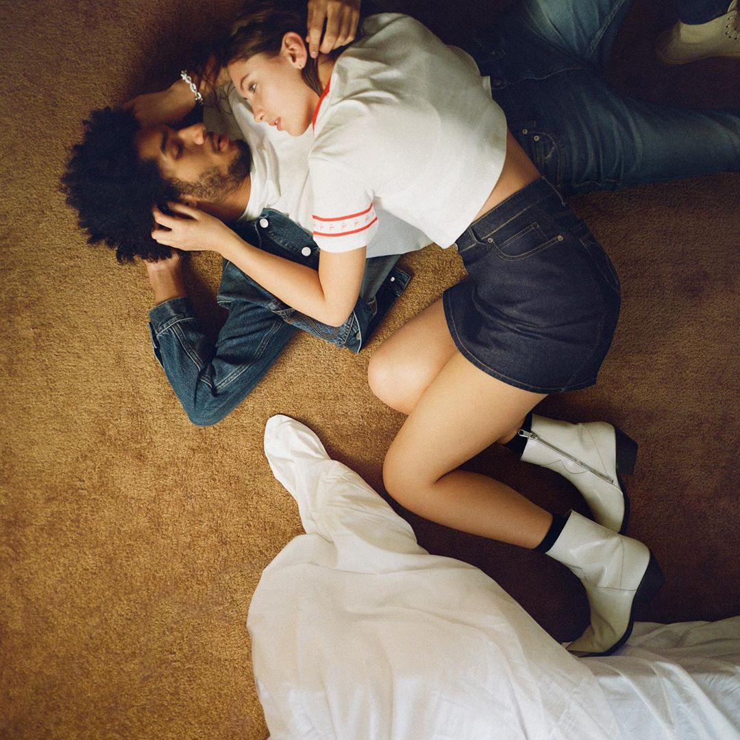 A casually posed couple lies on a brown carpet, the adult male resting on his back as the adult female rests on top of him.
