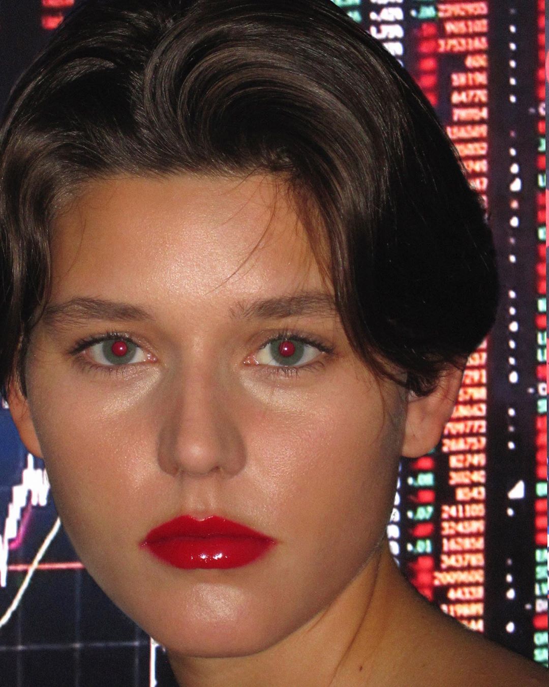 Close-up portrait of a woman with short dark hair and red lipstick, against a backdrop of stock market data.