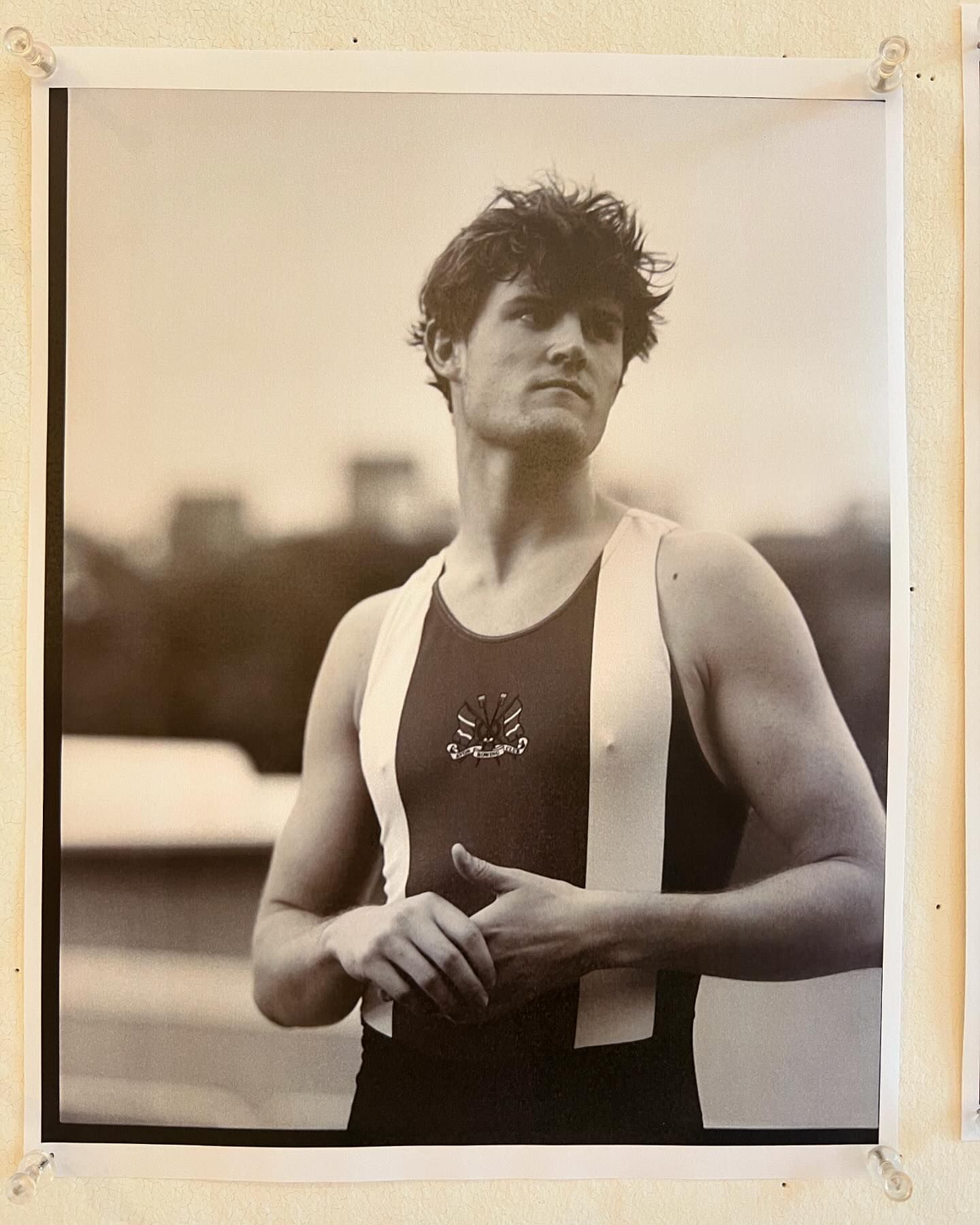 Black and white portrait of a young adult male rower in racing gear, set against an out-of-focus background. 
