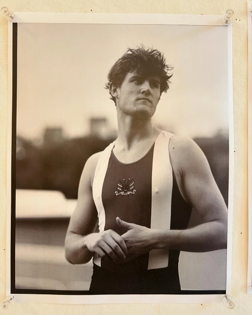 Black and white portrait of a young adult male rower in racing gear, set against an out-of-focus background. 