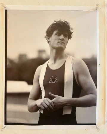 Black and white portrait of a young adult male rower in racing gear, set against an out-of-focus background. 