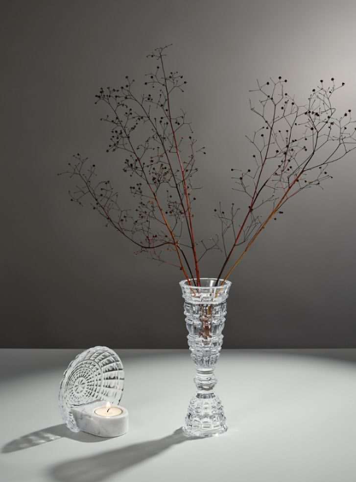 Elegant still life composition featuring a clear crystal vase holding dried branches, complemented by a candleholder on a white surface.