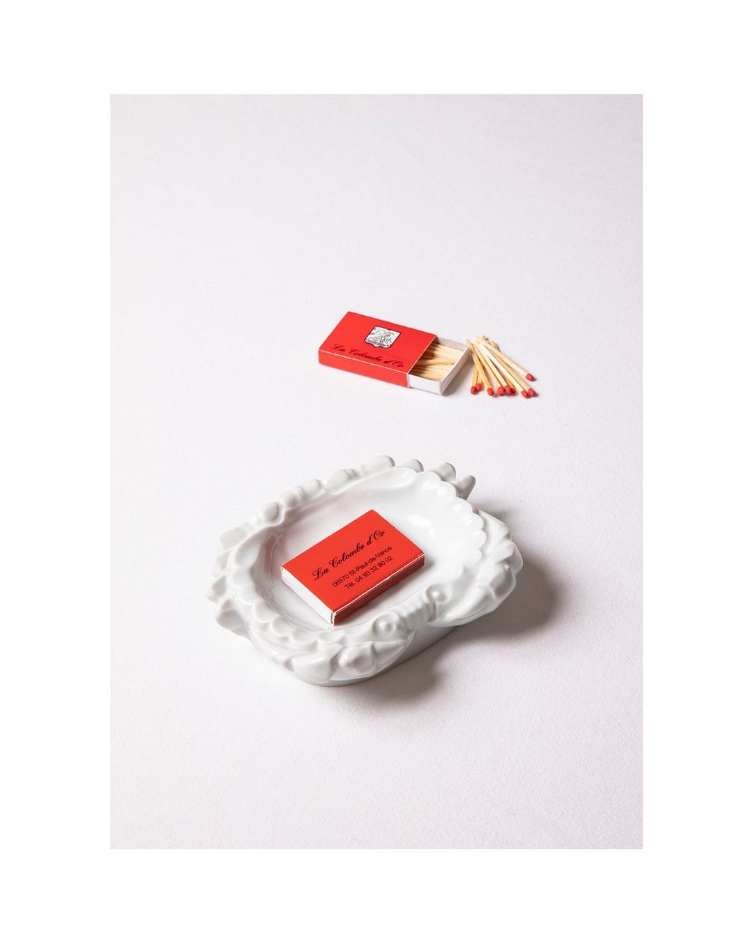 Still life studio shot of a small white dish with a red box of matches on top, along with a box of matches and scattered matches.