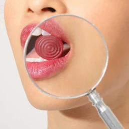 Close-up portrait of a woman holding a magnifying glass in front of her mouth while biting a red candy