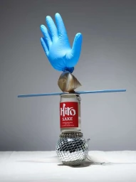 Balanced sculptural still life featuring a disco ball, a sake can, a sea shell, a blue stick, and a blue rubber glove.