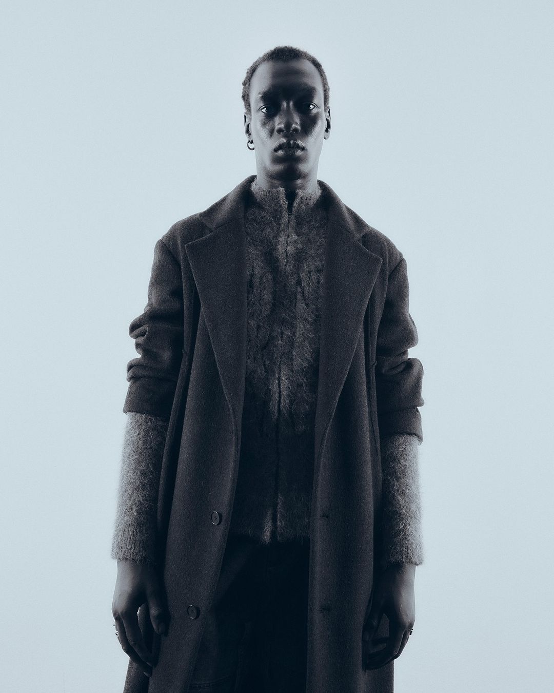 Portrait of a man wearing a dark textured coat and knitted cardigan against a light background by Theresa Kaindl