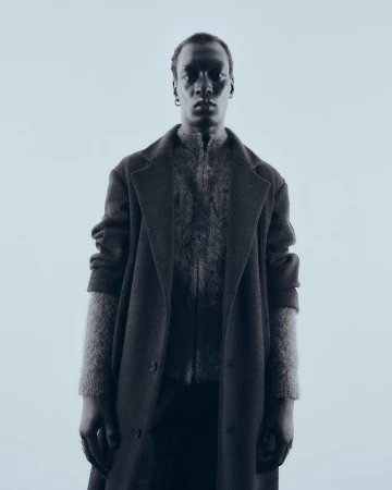 Portrait of a man wearing a dark textured coat and knitted cardigan against a light background by Theresa Kaindl