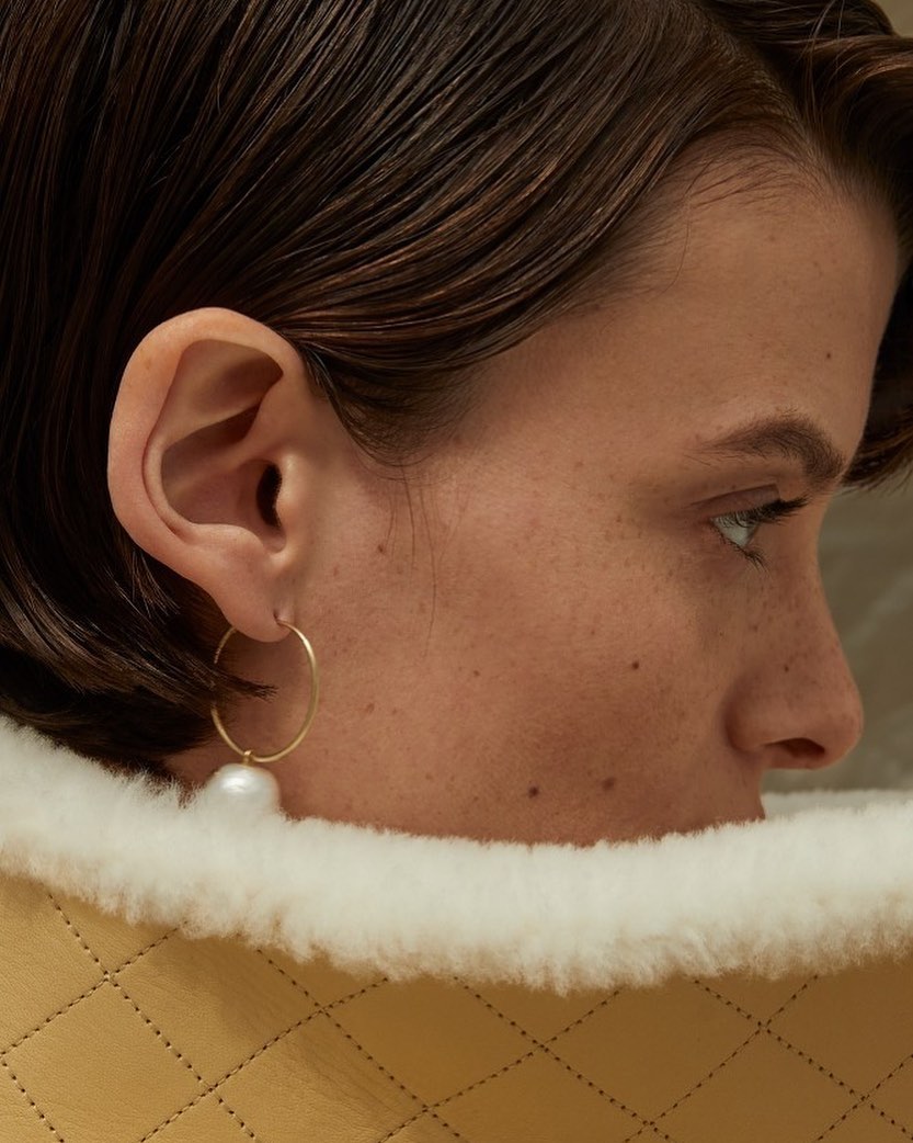 Adult woman's close-up profile featuring a pearl earring and stylish shearling collar, highlighting fashion and beauty.
