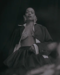 A woman wearing a white collared shirt, dark blazer, and crystal bra under dark moody lighting captured by photographer Theresa Kaindl.