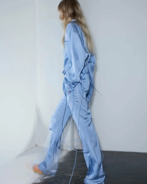 Fashion photo of a slender adult female model walking indoors, wearing a light blue striped pajama set and light orange shoes in a studio.