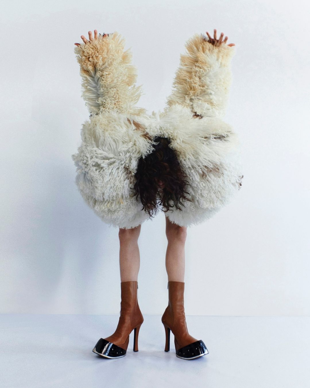 Fashion image of an unrecognizable person wearing a shaggy white and brown outfit and high-heeled boots against a white backdrop.