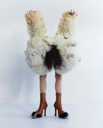 Fashion image of an unrecognizable person wearing a shaggy white and brown outfit and high-heeled boots against a white backdrop.