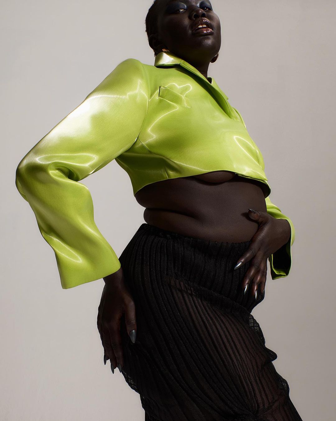 A Black woman poses wearing a green crop top and a sheer skirt. A fashion shot with a high angle and studio lighting. Beauty and glamour.