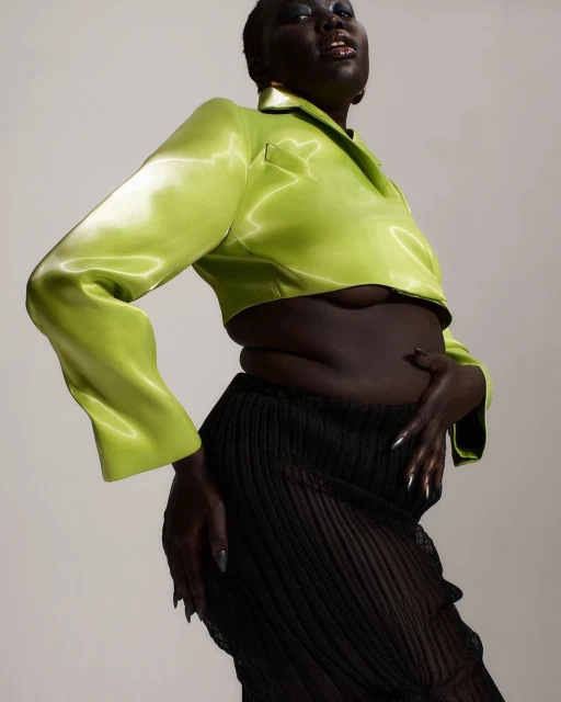 A Black woman poses wearing a green crop top and a sheer skirt. A fashion shot with a high angle and studio lighting. Beauty and glamour.