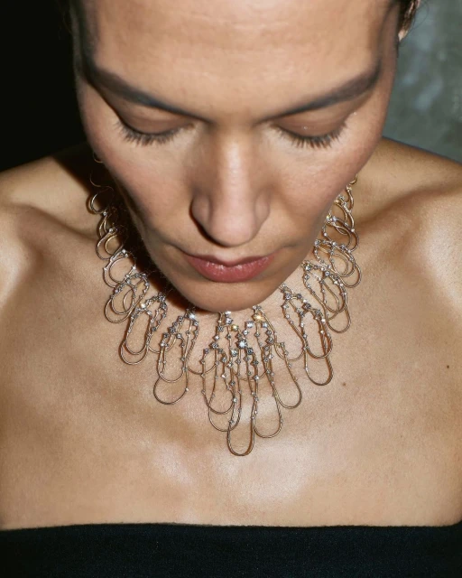 Close-up studio shot of an adult woman wearing a metallic necklace with clear gemstones, focusing on her face and jewelry.