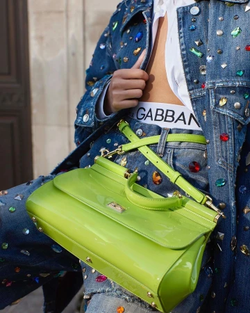 Close-up of a person wearing an embellished denim jacket, jeans, and holding a glossy lime green handbag by Theresa Marx