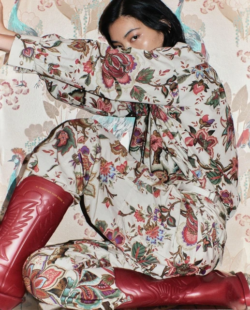 Asian woman poses in a floral-patterned outfit and red boots against a wallpaper backdrop featuring a similar floral design.