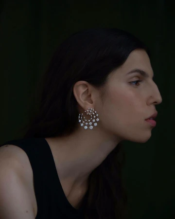 Profile portrait of a woman wearing an intricate diamond earring and black top against a dark background