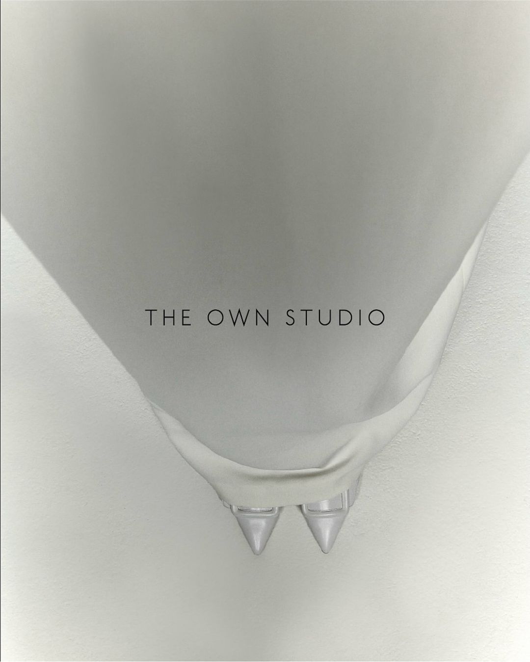 Overhead studio shot of white bridal stiletto heels with pointed toes, shiny finish and ankle straps, against a light gradient backdrop.