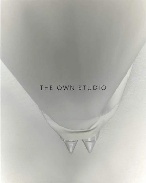 Overhead studio shot of white bridal stiletto heels with pointed toes, shiny finish and ankle straps, against a light gradient backdrop.