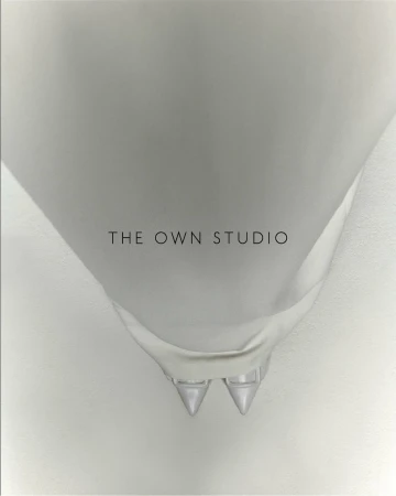 Overhead studio shot of white bridal stiletto heels with pointed toes, shiny finish and ankle straps, against a light gradient backdrop.