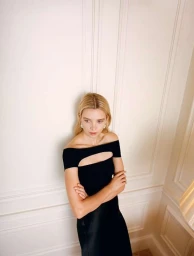 Blonde woman wearing a black off-the-shoulder top leaning against a white panelled wall in a portrait by Theresa Marx