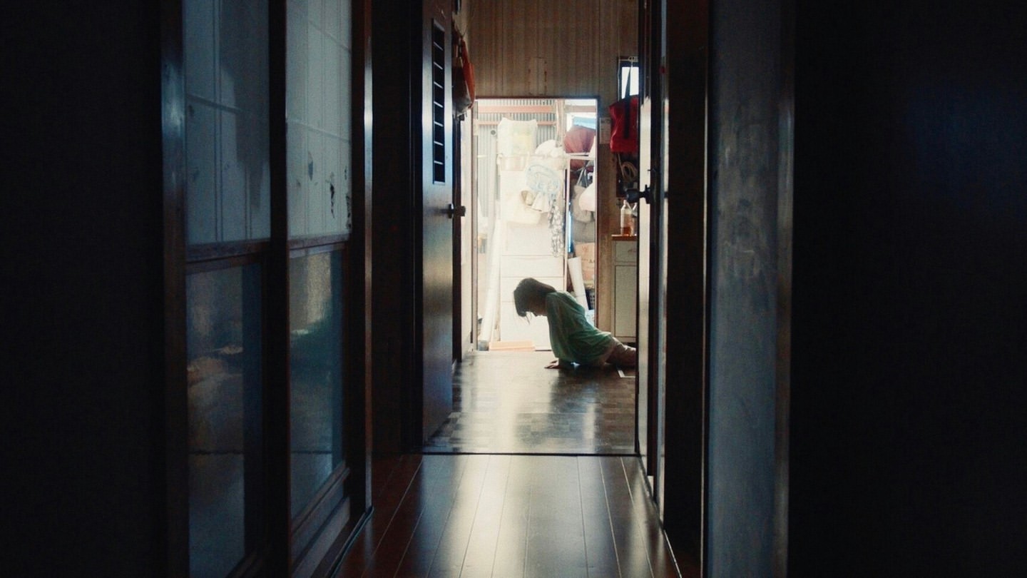 Person doing push-ups in a dimly lit hallway, seen through doorways. The background shows an open kitchen area with items.