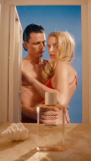 Coco Mademoiselle perfume ad featuring a shirtless man and a blond woman in a red swimsuit framed by a white structure with blue sky.