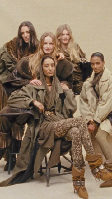 Group portrait of five fashion models in earth-toned clothing, posing in front of a neutral backdrop in a studio setting, showcasing textures and patterns.