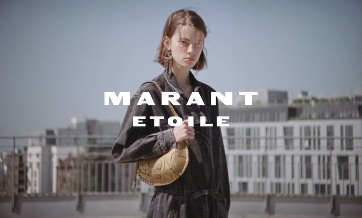 A young woman in a denim jumpsuit stands outdoors with a crescent-shaped handbag in front of an urban background and fashion text overlay.