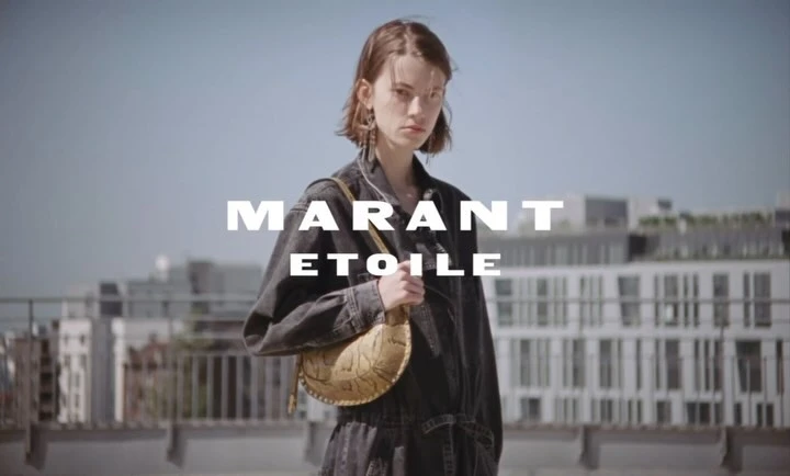 A young woman in a denim jumpsuit stands outdoors with a crescent-shaped handbag in front of an urban background and fashion text overlay.