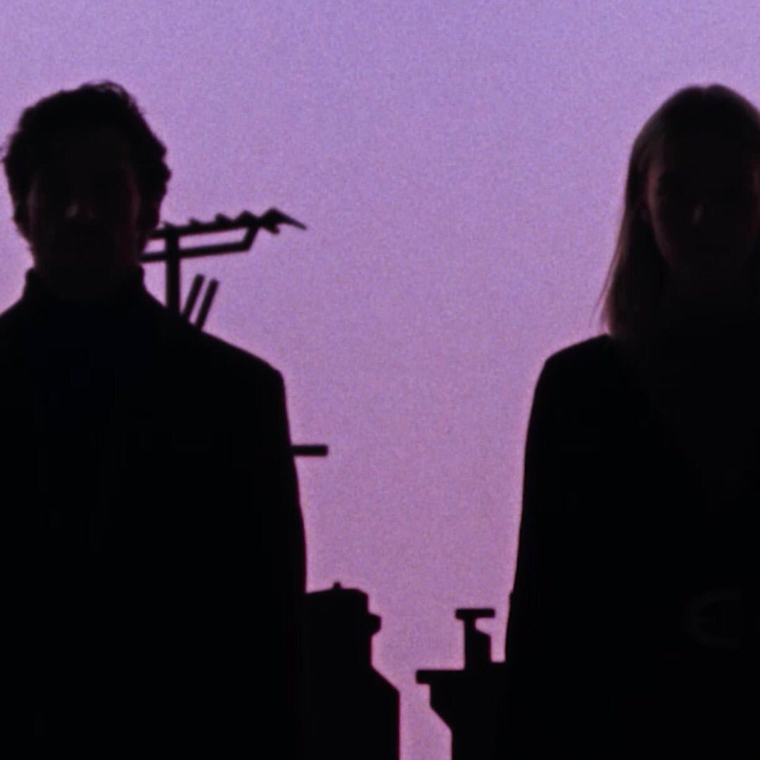 Silhouetted couple against a purple sky, architectural details visible on the left side of the frame, creating a stark contrast.
