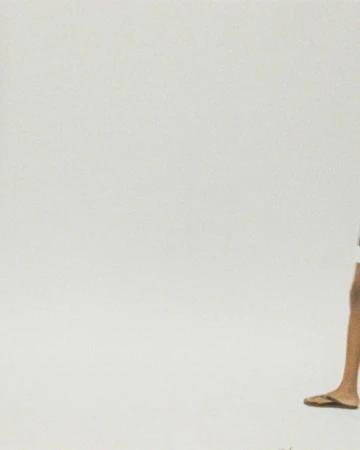 Partial view of an adult with dark hair, wearing shorts and flip-flops, stands against a plain white background, creating a minimalistic fashion shot.