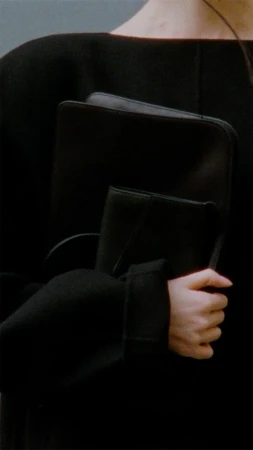 Mid-shot of an adult female holding a black portfolio, wearing a dark top with sleeves, showing hands and minimalist fashion.