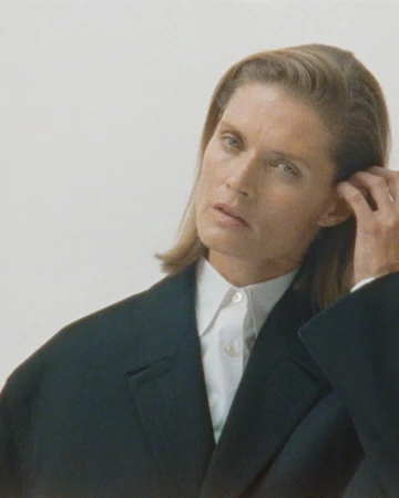 Portrait of a woman with medium brown hair wearing a dark blazer and white button shirt against a plain light background