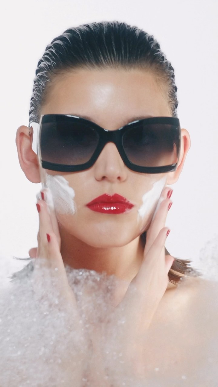 Glamorous beauty portrait of a woman with red lipstick and sunglasses in bubbly water, showcasing skincare and fashion.