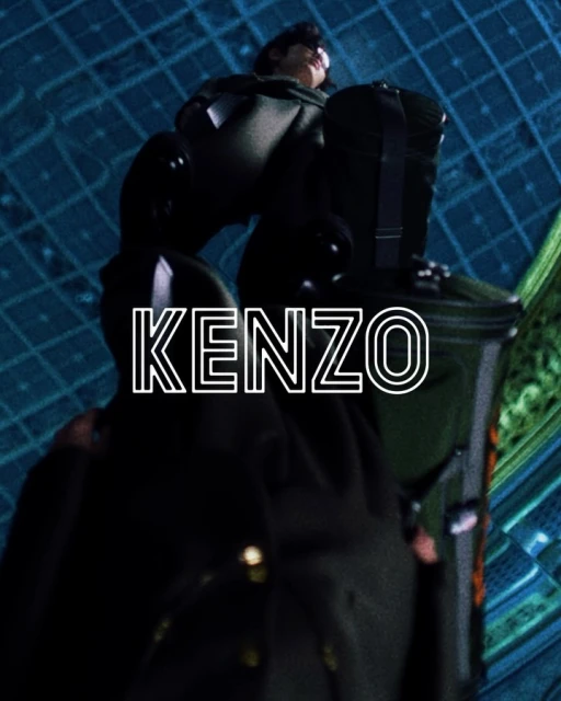 Eye-level shot of a person with short dark hair wearing a black jacket with buttons against a blue and green background.