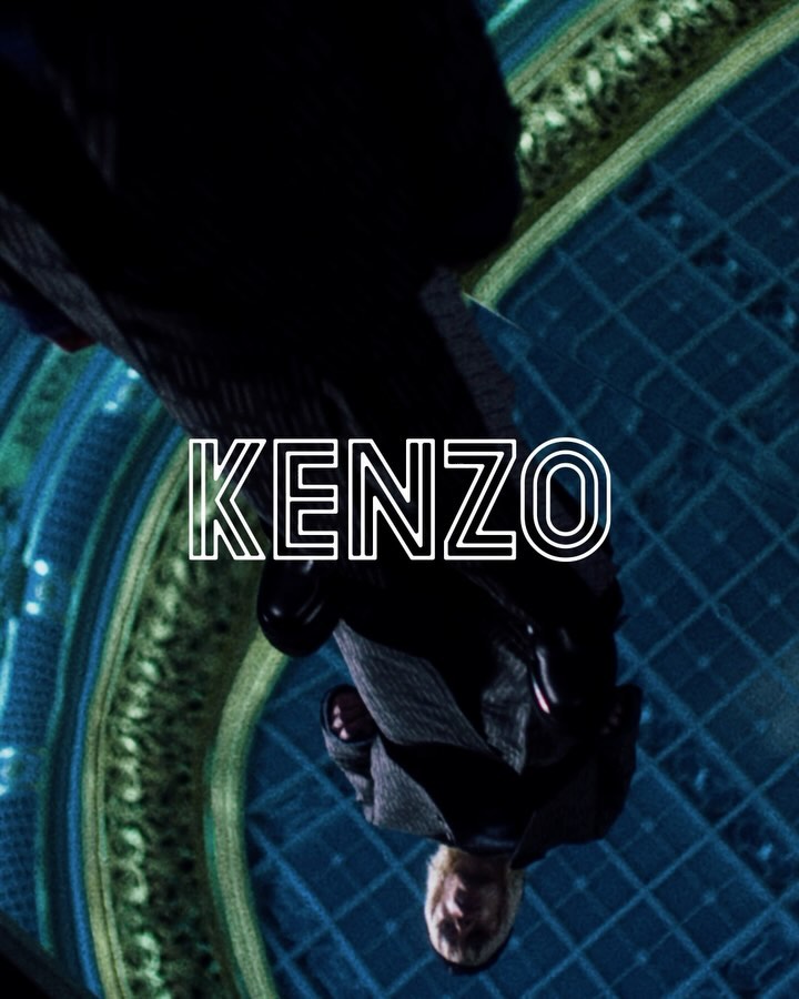 Upside-down shot of a man wearing a dark suit indoors, with the name 'KENZO' overlaid in white against a blue tiled background.