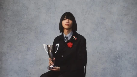 A young man with dark shoulder-length hair holding a silver trophy in a studio portrait by photographer Thibault Della Gaspera