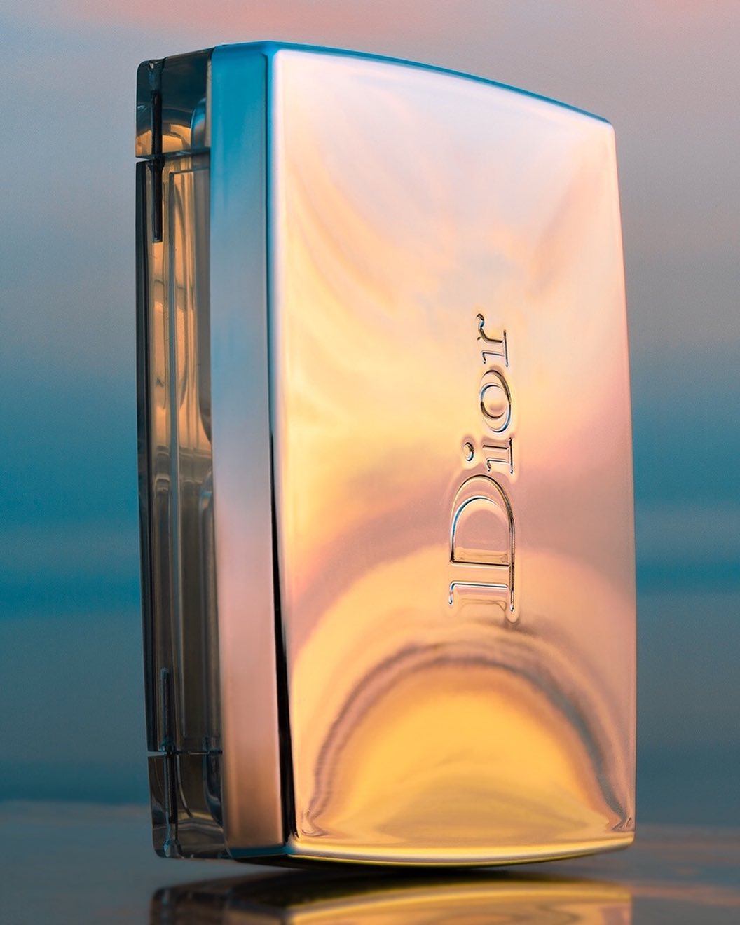 Elegant studio shot of a gold-toned Dior perfume bottle. The bottle has a sleek, rectangular design that showcases luxury and sophistication.